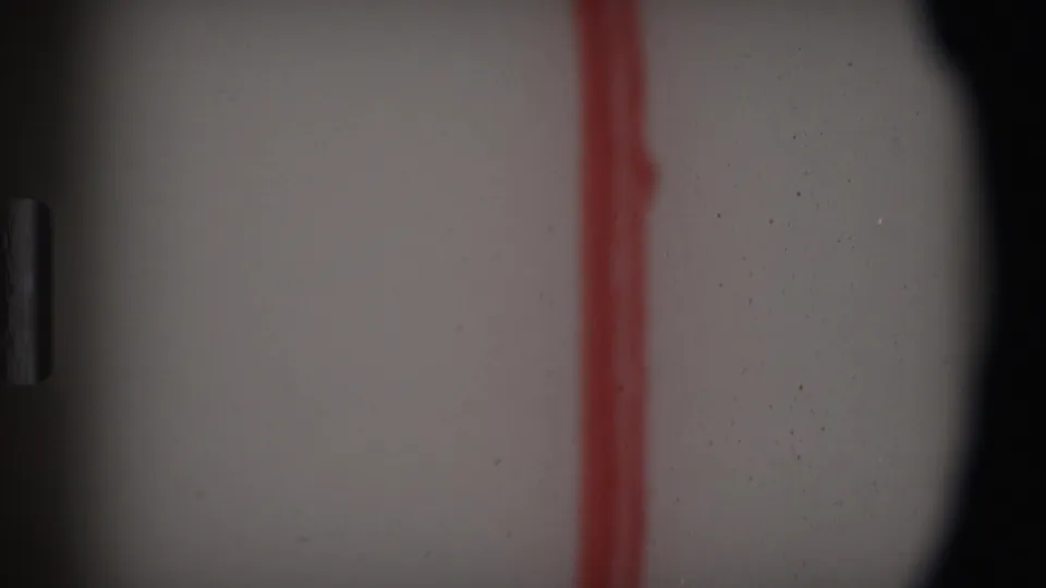 1969 Angola-attributed 8mm frame showing a pale surface crossed by a red vertical mark, with dark frame edges, grain, and dust.