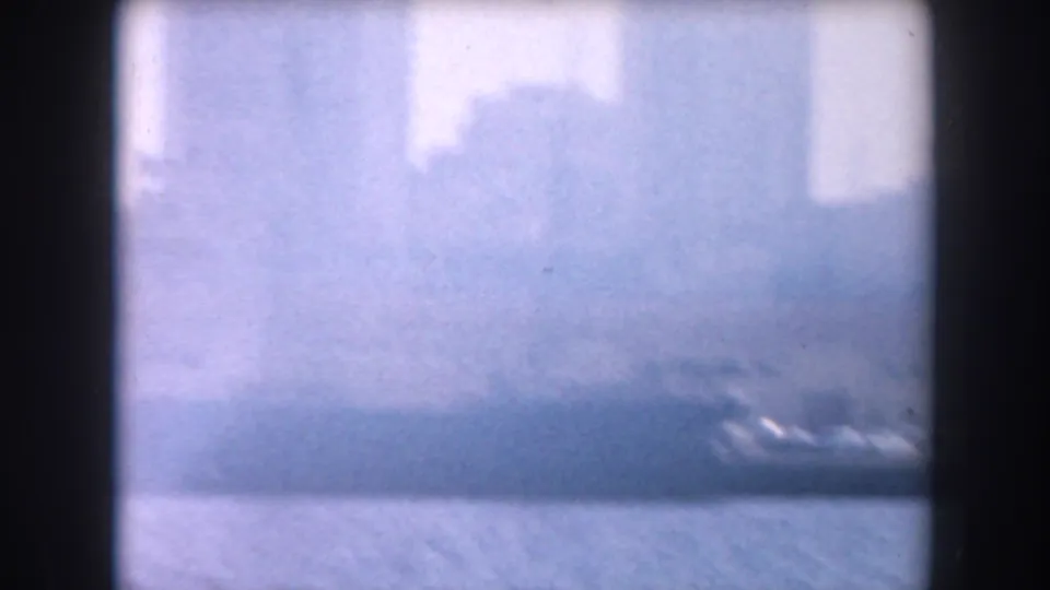 1961 California 8mm frame showing a hazy waterfront with water in the foreground and indistinct city buildings beyond.