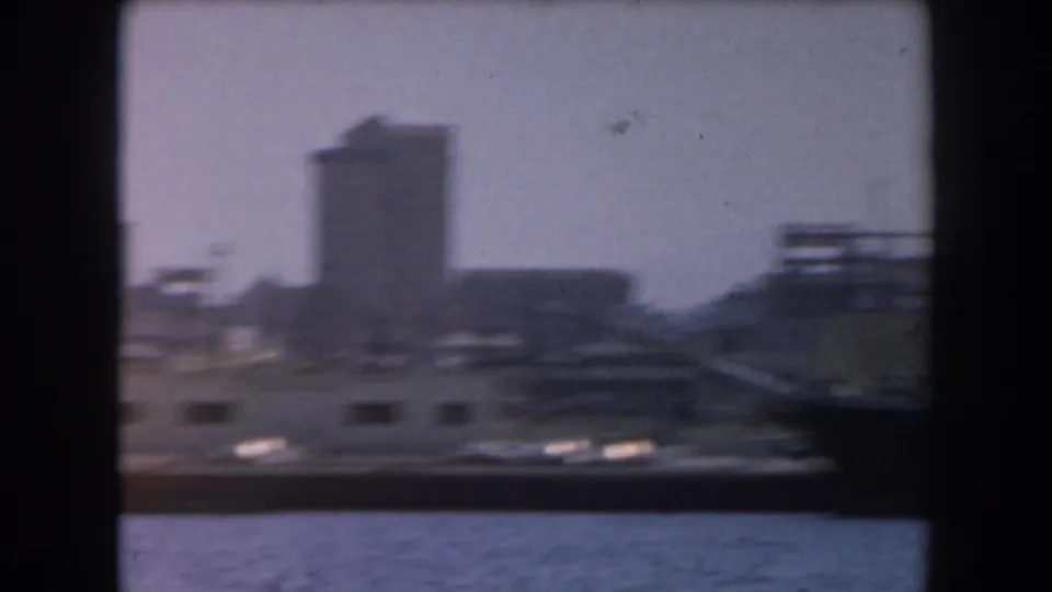 1961 California 8mm frame showing a docked ship or waterfront structure with buildings and a tower-like form behind it.