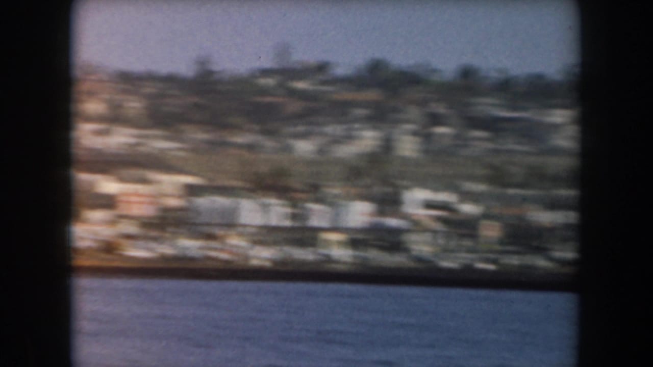 Hillside town and shoreline buildings viewed across blue water.