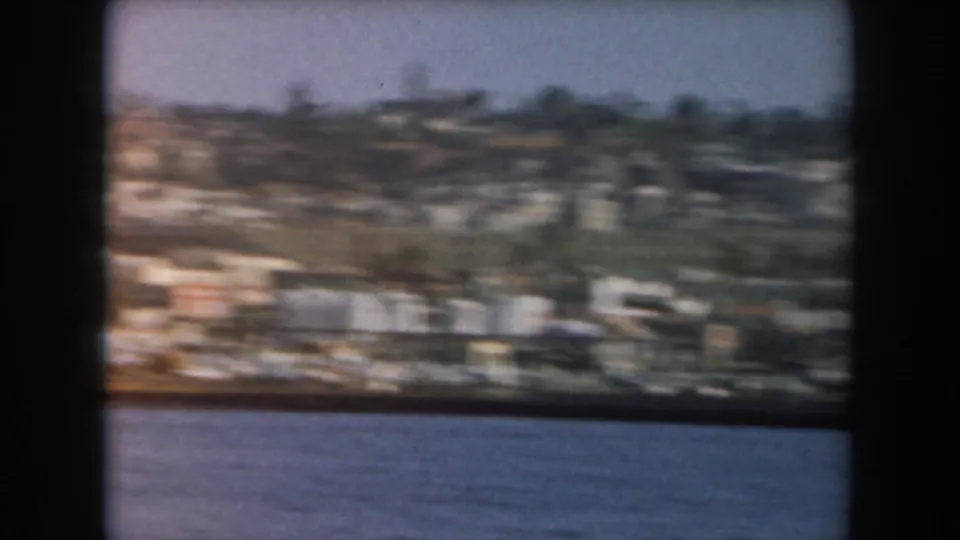 1961 California coastal frame with hillside homes and low waterfront structures seen from across the water.