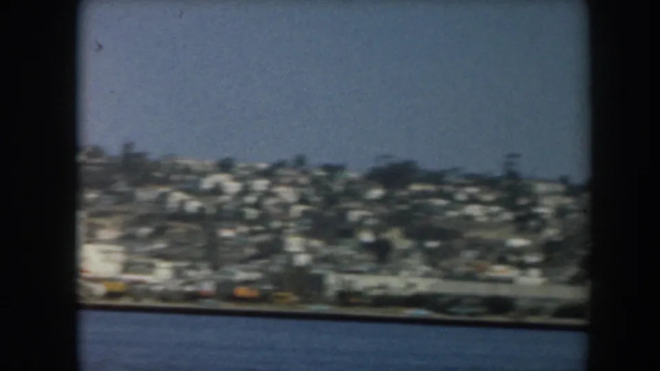 1961 California coastal shoreline and blue water viewed from a moving vessel through dark frame bars.