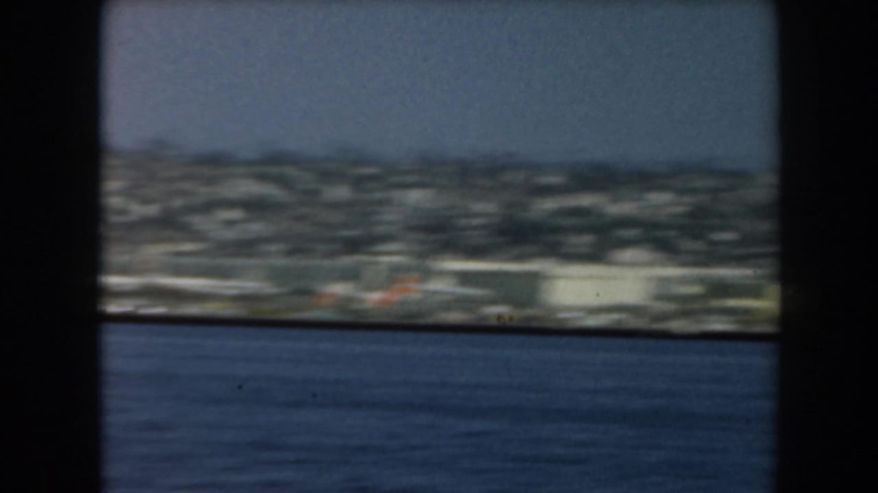 Coastal buildings and water framed by dark window or vessel structure.