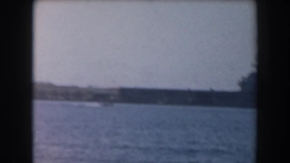 A large grey naval-looking ship appears in the distance across California coastal water in 1961 home-movie footage.