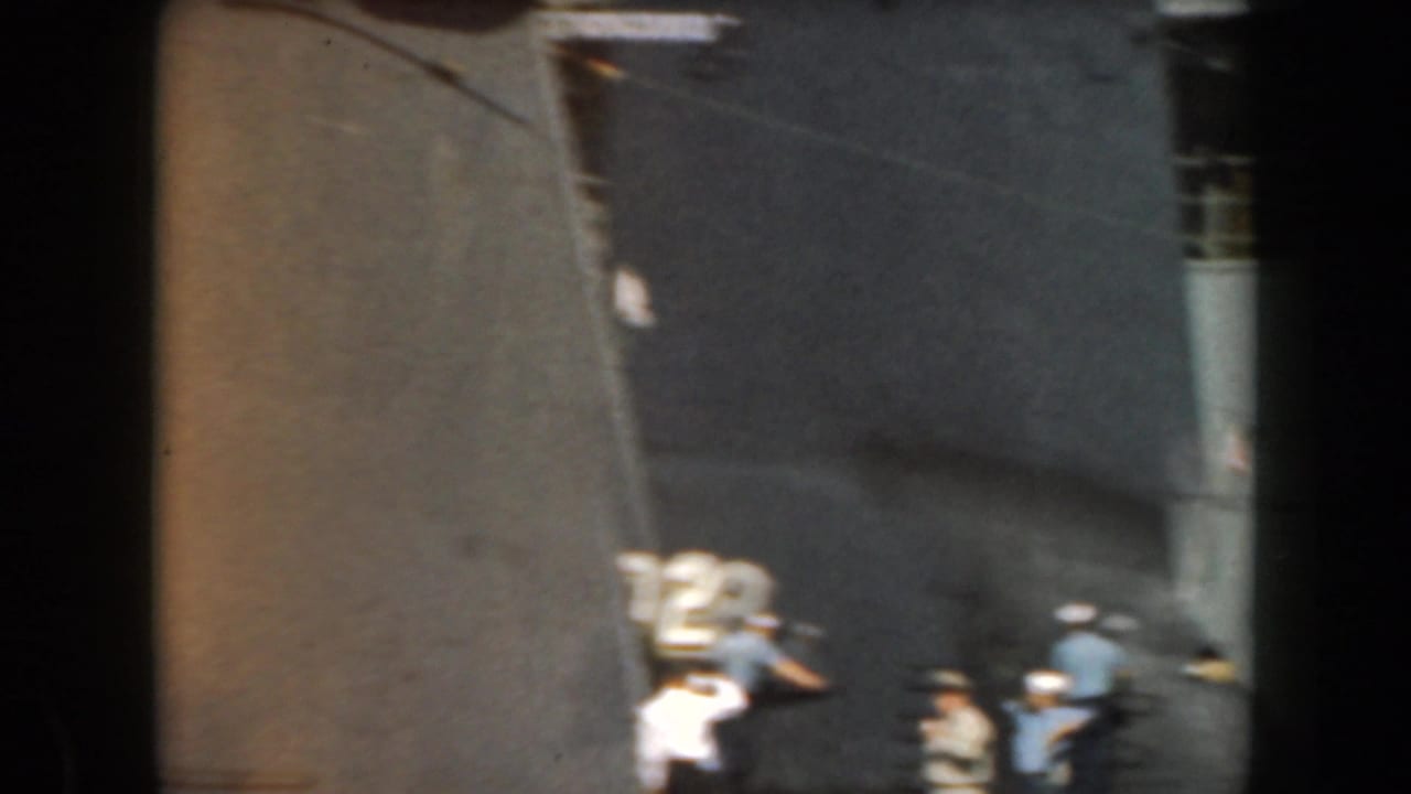 1961 California port view of uniformed naval crew near a dark ship hull, railings, and deck-side equipment.