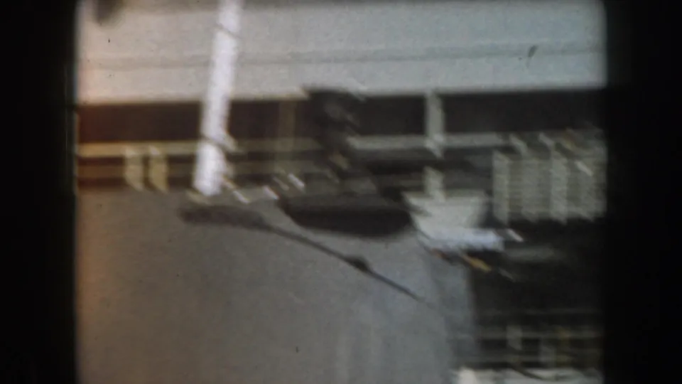 Soft 8mm frame from 1961 California showing a close section of a grey naval ship with railings, pipes, shadowed structure, and a mooring line.