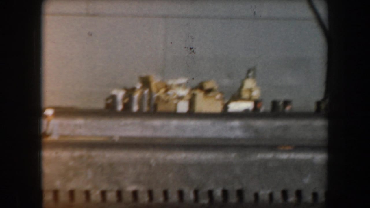 1961 California home-movie frame of a grey boat with clustered deck equipment, filmed from close range on the water.
