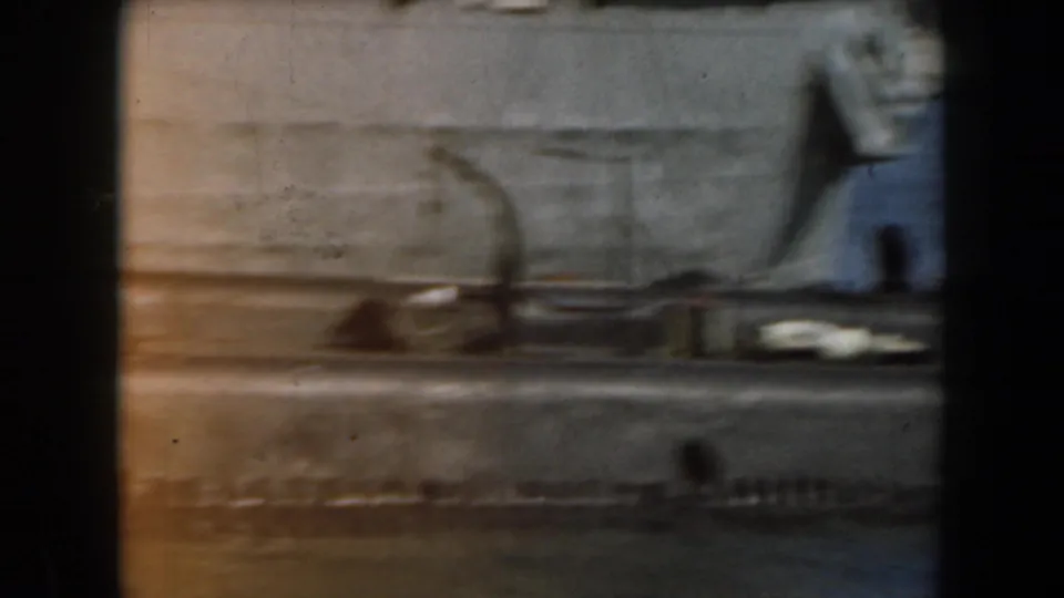 Blurred 1961 California 8mm view of the side of a grey boat, with hull lines and deck shapes passing in close view.