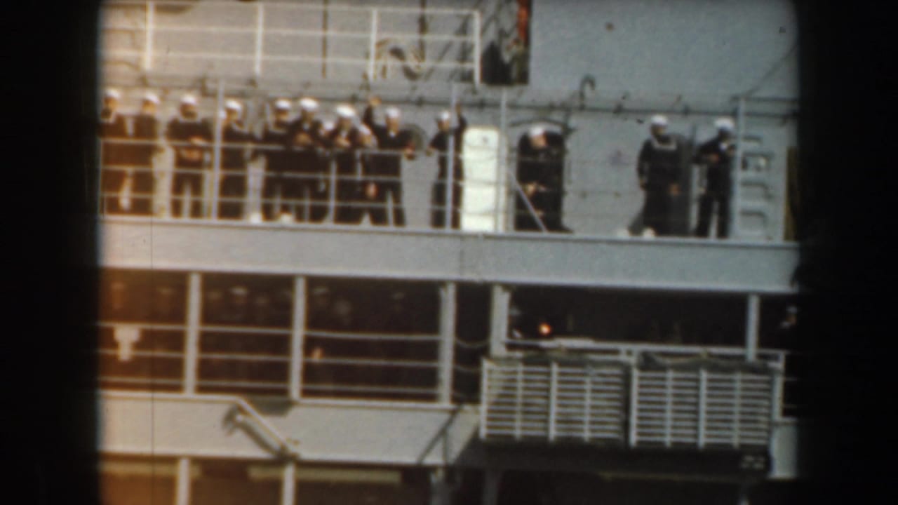 Sailors in white uniforms stand along the railings of a ship deck.