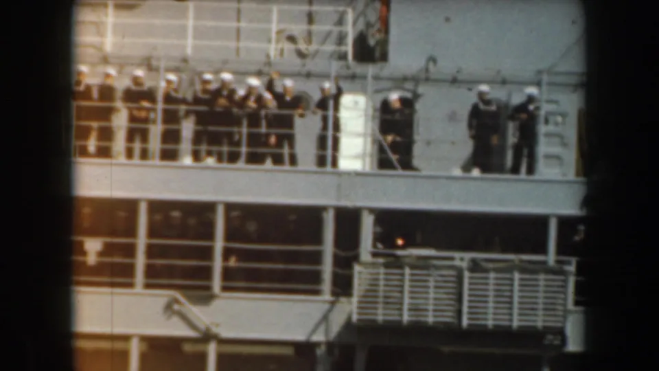 1961 California home-movie frame showing sailors in white uniforms gathered on the deck of a naval vessel.