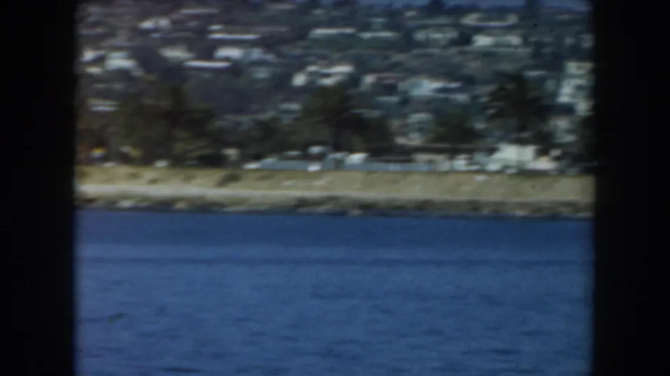 Soft 8mm view of a California shoreline, with trees and hillside homes seen across blue water.