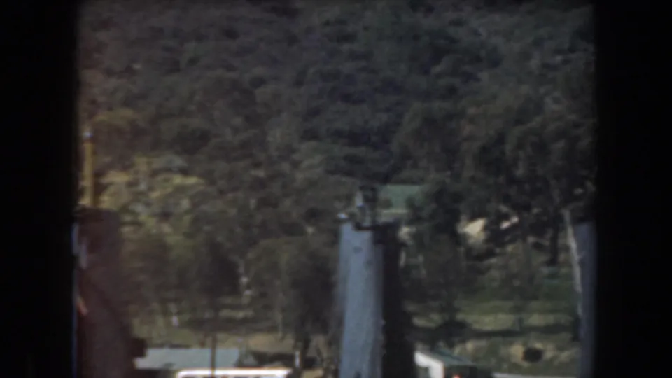 Soft 8mm frame of a California hillside waterfront, with dark foreground posts and a pale dockside structure below.