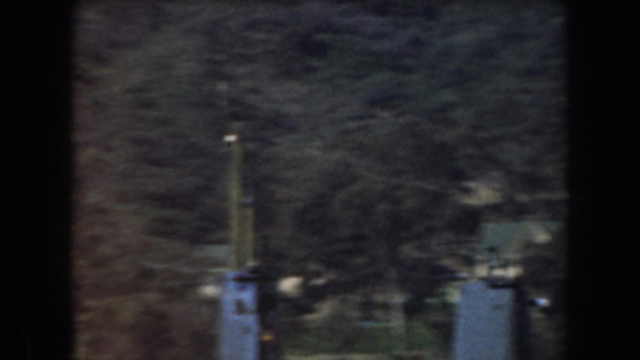 1961 California 8mm frame showing blurred boat structures below wooded hills, partly obscured by dark vertical film or window framing.
