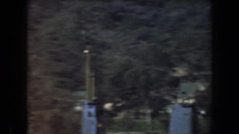 1961 California 8mm frame showing blurred boat structures below wooded hills, partly obscured by dark vertical film or window framing.