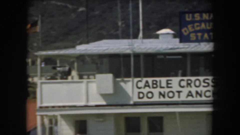 1961 California 8mm frame showing the U.S. Naval Degaussing Station sign and a banner reading cable crossing do not anchor.