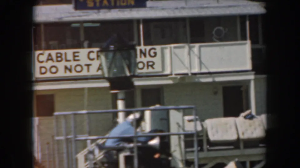 1961 California harbor view showing a naval station structure, cable crossing warning, dock railings, and a small boat.