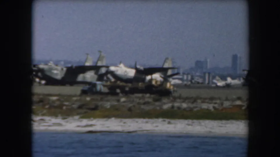 A 1961 California 8mm view of several military aircraft on coastal ground, backed by a distant skyline.