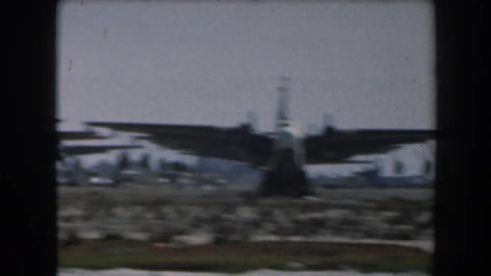 Rear-facing view of a parked propeller aircraft on a dusty waterside airfield in 1961 California footage.