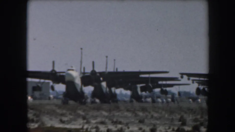 Multiple propeller aircraft appear parked in rows on a flat California airfield near water, filmed on 8mm in 1961.