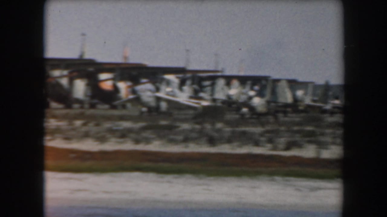 Row of small propeller aircraft near a hangar or covered airfield structure.