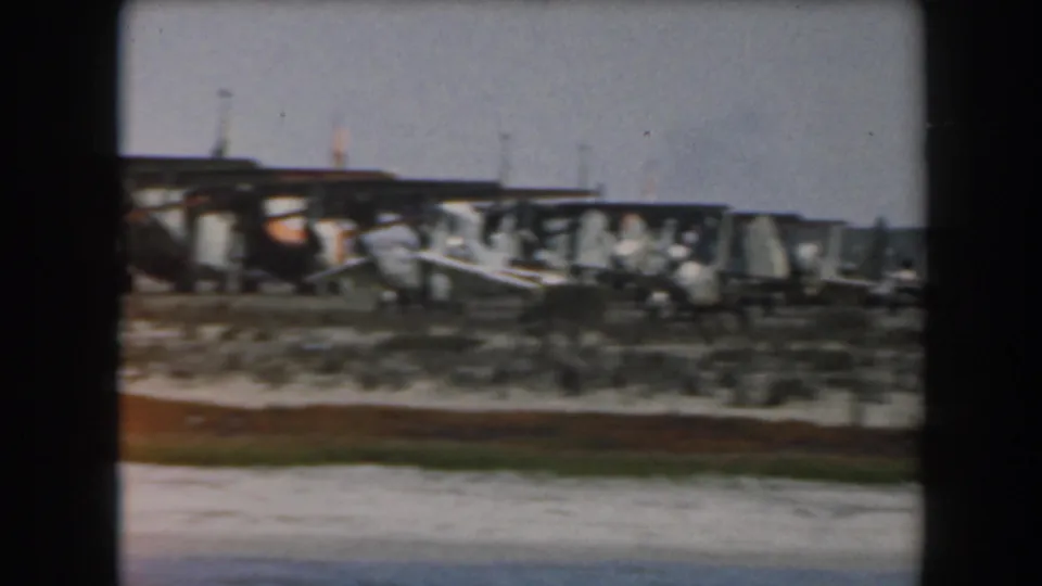 Distant 1961 California airfield view with several small propeller planes lined up near a low hangar structure.