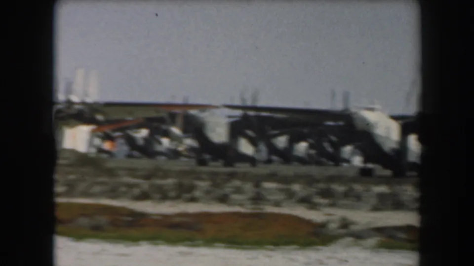 Side view of a large military transport aircraft on a California airfield, filmed at a distance on 8mm in 1961.