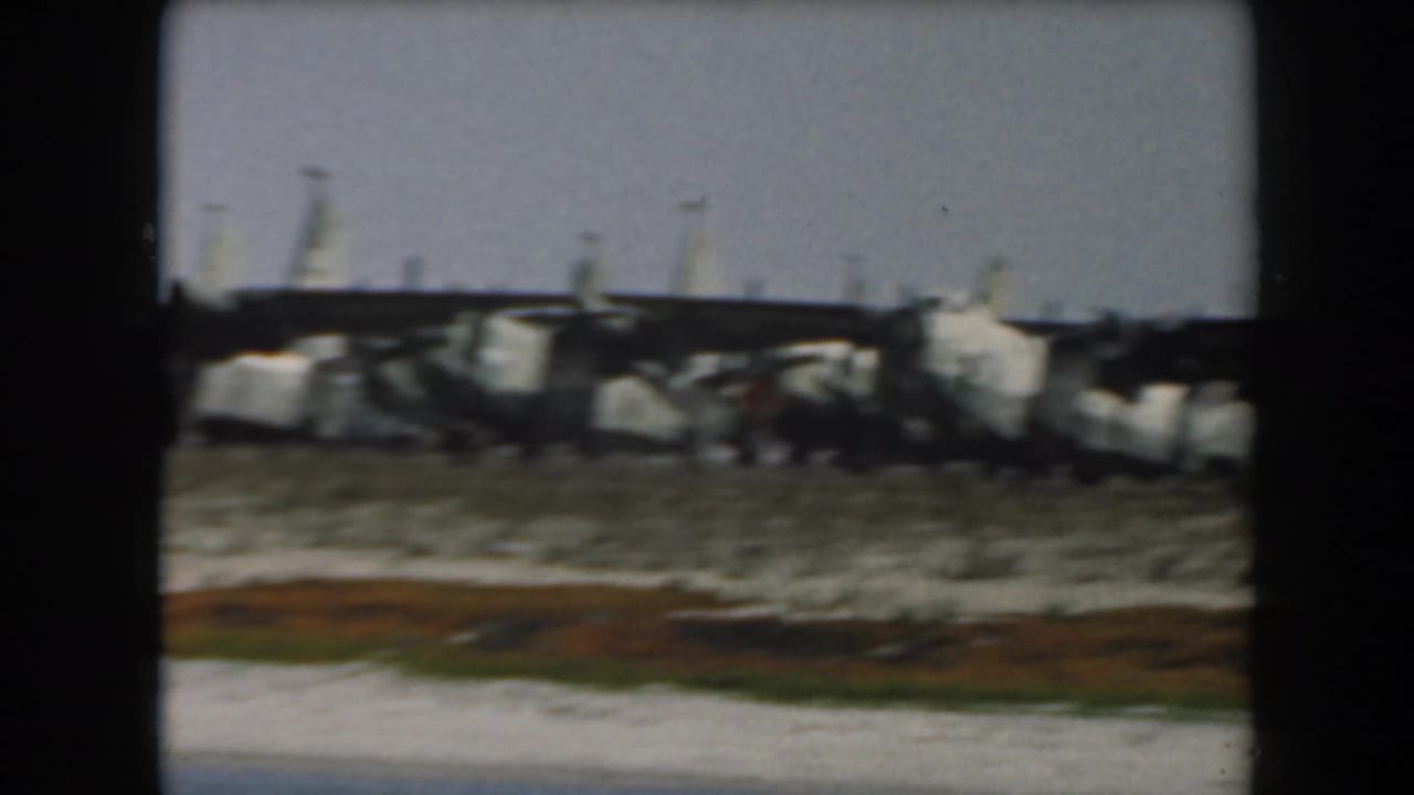 Derailed rail cars lie along a sandy shoreline with water in the foreground.