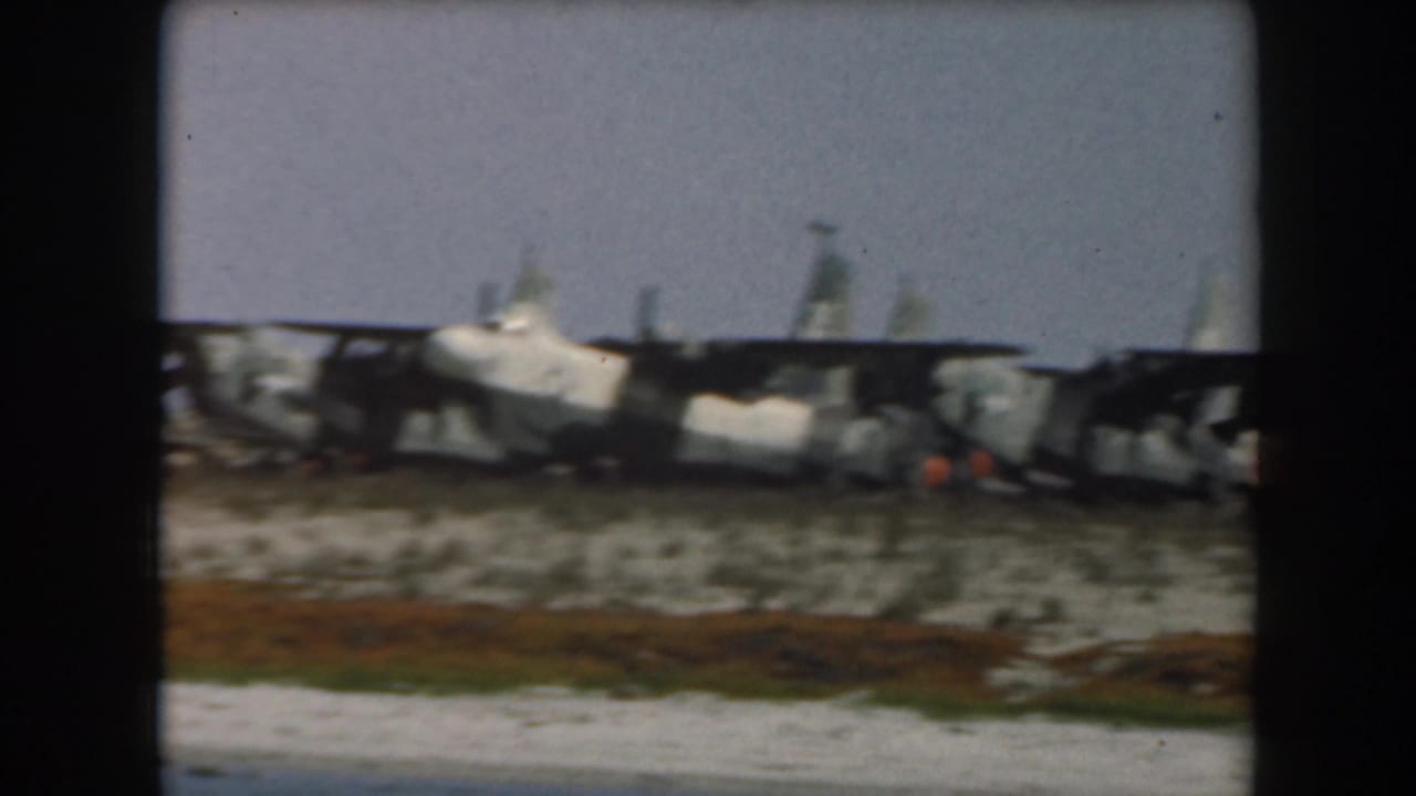 Damaged train cars rest beside pale sand with a small orange detail near the wreckage.