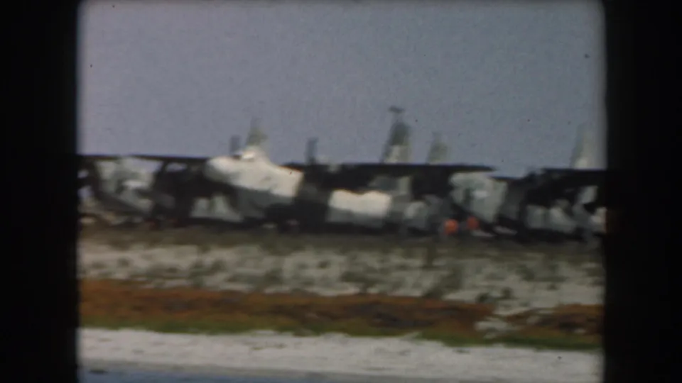 1961 California home-movie frame of a coastal rail wreck, with derailed cars and an orange-colored detail near the debris.