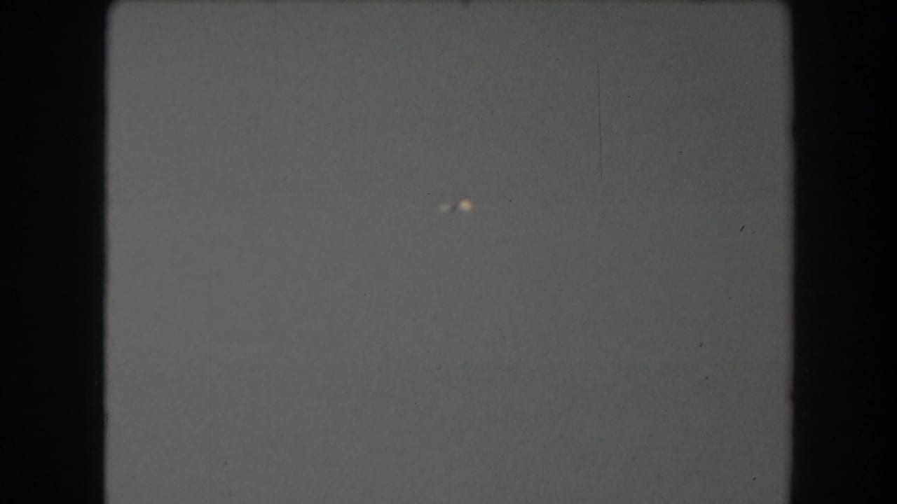 Mostly blank pale film frame with dark gate edges and small light specks.