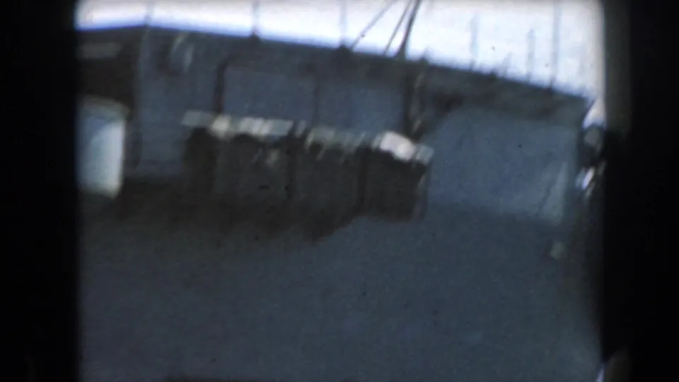 The camera passes along the ship side, showing deck structure, rigging lines, pale hull surfaces, and heavy 8mm frame edges.