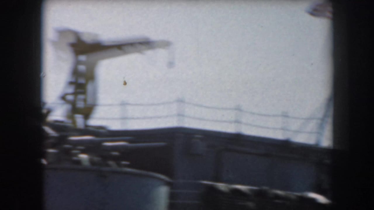 Blurred grey ship superstructure with deck railing and a crane-like mast against a pale sky.