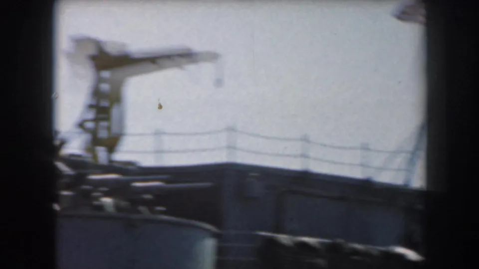 1961 California 8mm frame showing a distant grey naval vessel with railings and mast equipment under a bright sky.