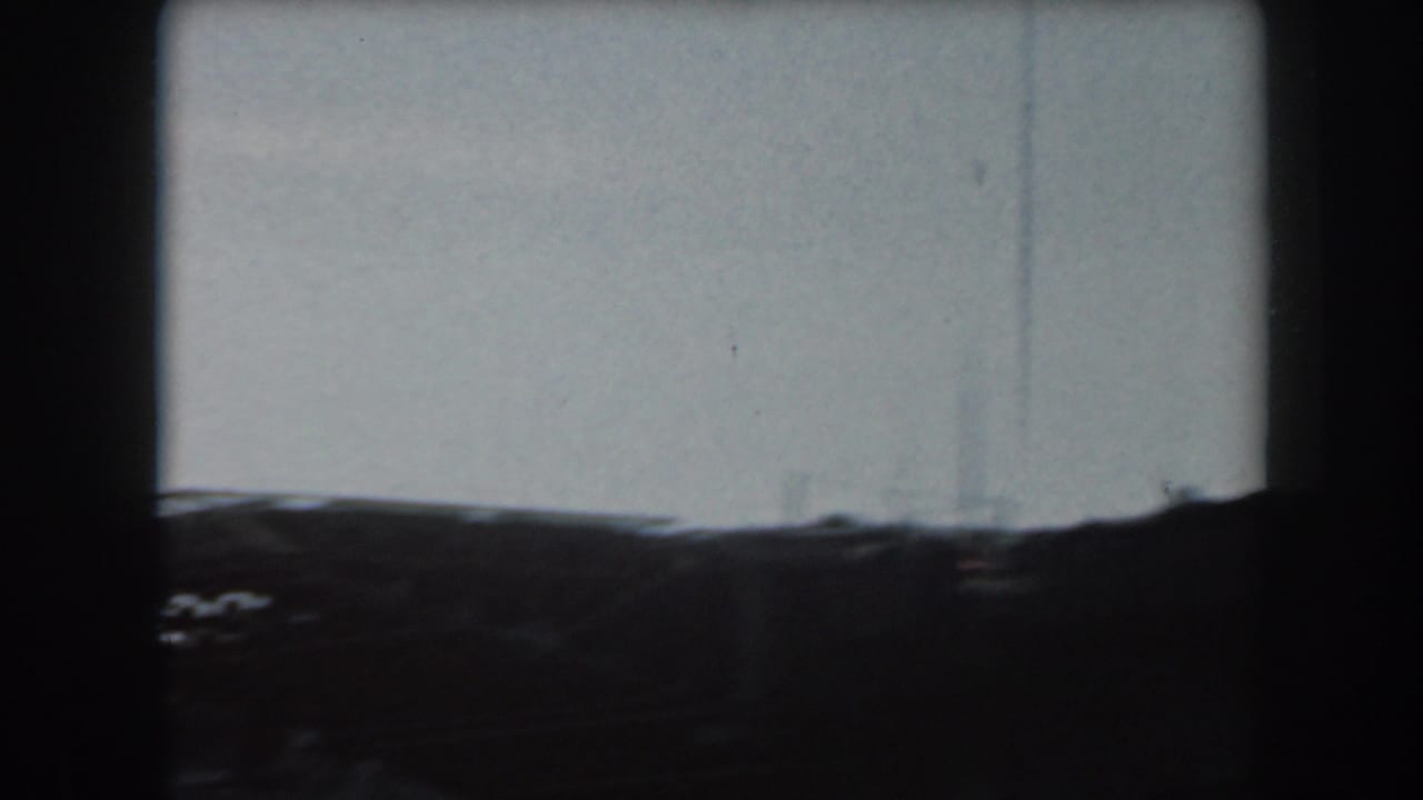 1961 California home-movie frame showing a dark, distant naval vessel form against a pale sky with heavy film borders.
