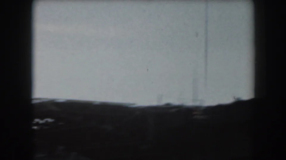 1961 California home-movie frame showing a dark, distant naval vessel form against a pale sky with heavy film borders.
