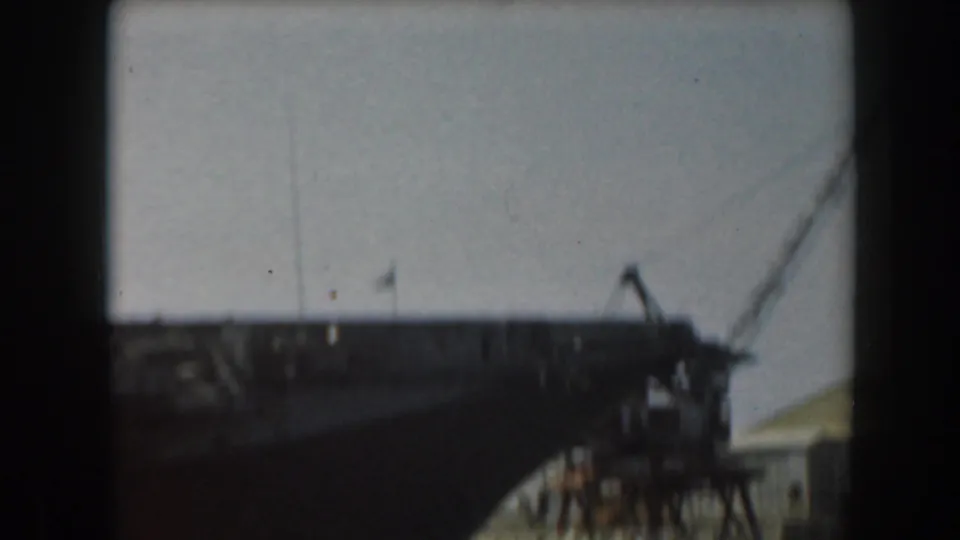 1961 California frame with the upper structure of a large military sea vessel and angled rigging or crane lines against sky.