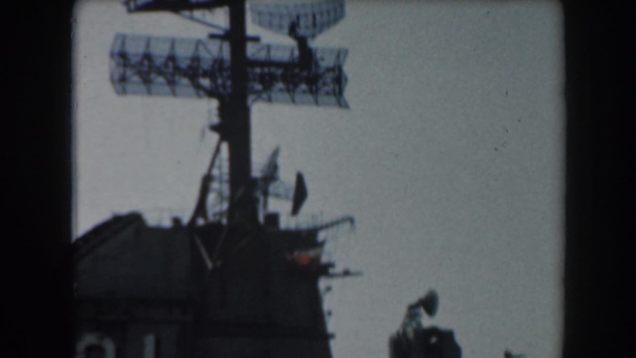 Dark naval superstructure with radar array and antennas against a pale sky.