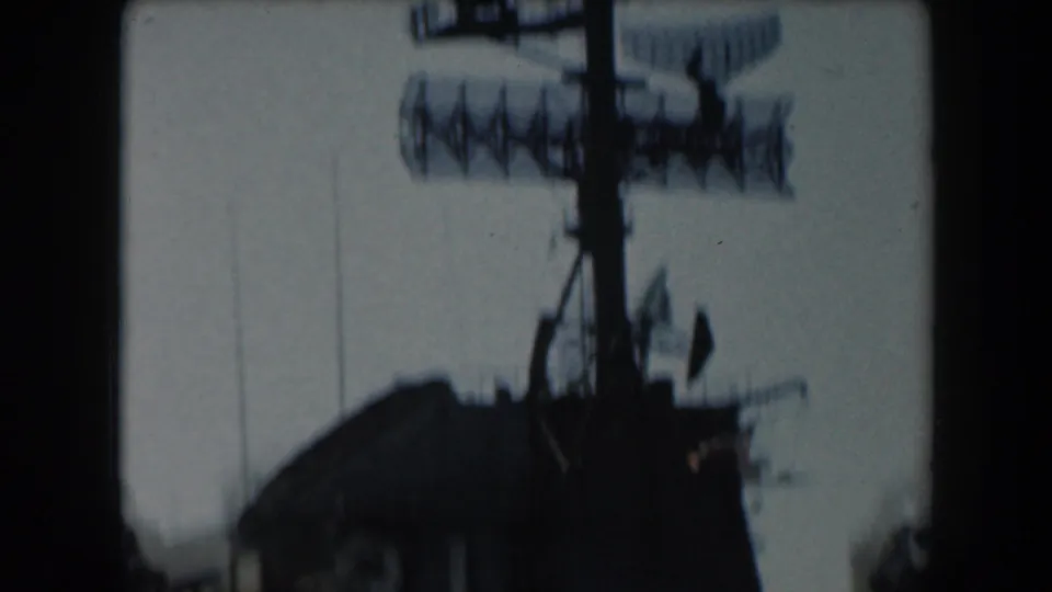 Soft 1961 8mm view of a naval mast with radar equipment and antennas silhouetted against a bright sky.