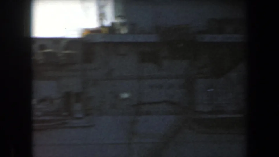 Handheld 8mm frame showing a blurred section of a gray naval vessel with deck edges and dark structural forms.