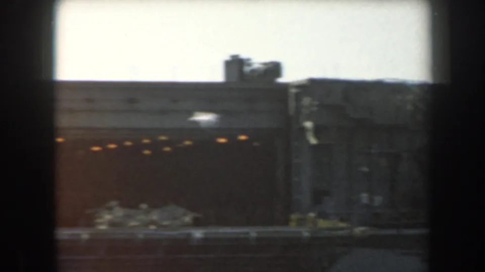 1961 California home-movie frame showing a gray warship hull section, small lit openings, and a bright sky beyond.