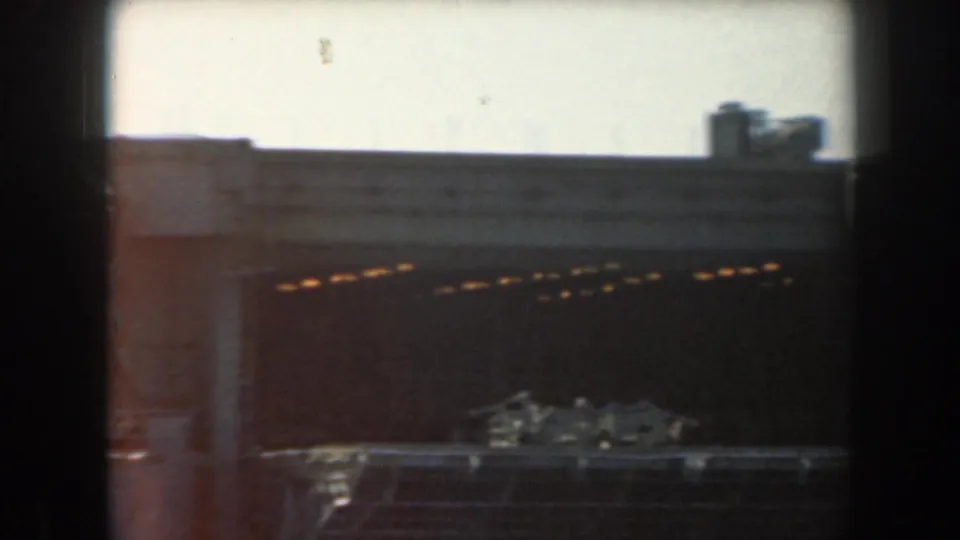 1961 California 8mm frame showing a dim industrial tunnel or passage with warm lights, pale wall surfaces, and heavy dark borders.