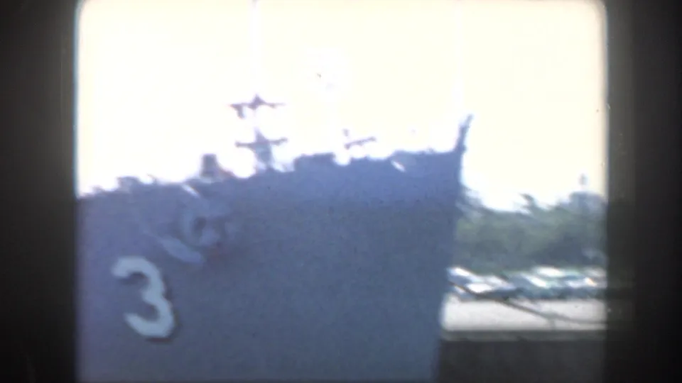 1961 home-movie frame showing a grey battleship section with a large painted number and flag near the superstructure.