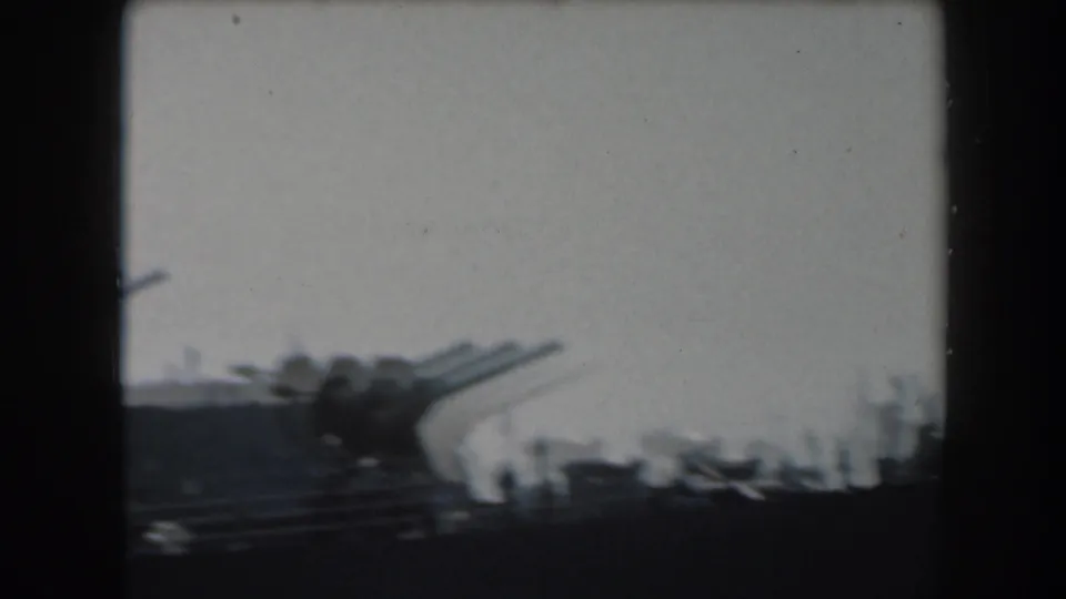 A soft 8mm California view of large battleship guns extending from a dark deck silhouette.