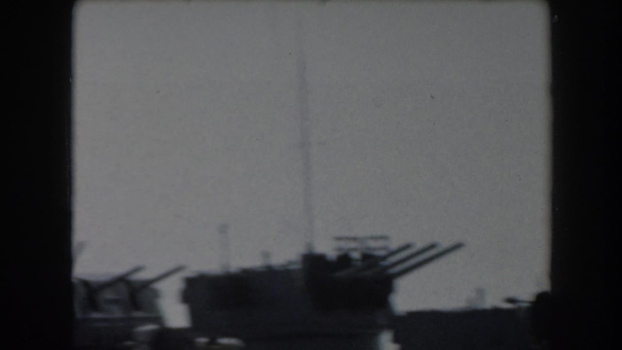 1961 California 8mm frame showing dark shipboard gun barrels and mast details silhouetted against a bright sky.