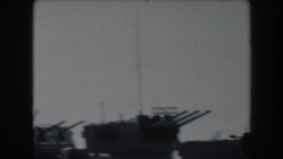 1961 California 8mm frame showing dark shipboard gun barrels and mast details silhouetted against a bright sky.