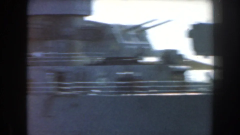 Blue-tinted 8mm frame with glare and motion blur across a ship deck or dockside naval form in a California harbor.