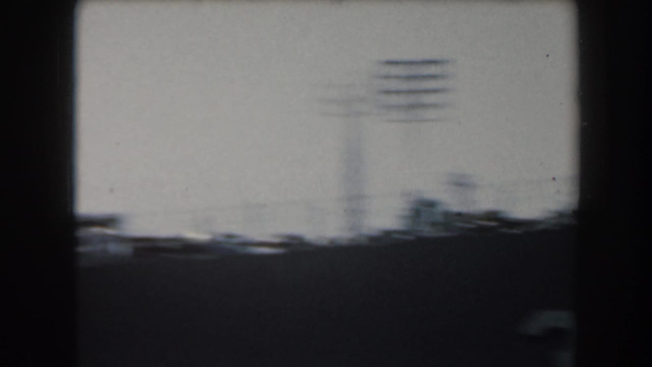 Dark ship profile with antenna masts and a blurred waterfront beyond the deck line.