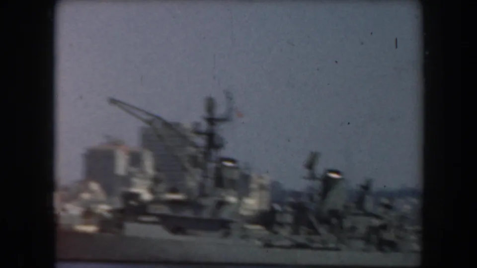 1961 California home-movie frame showing a grey ship near a hazy waterfront skyline from a moving vessel.
