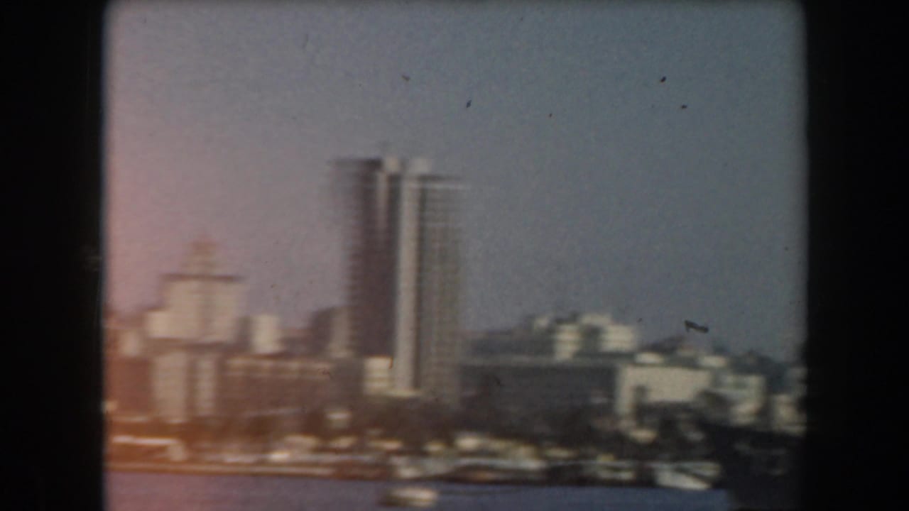 Tall white city buildings rise along a waterfront under a hazy sky.