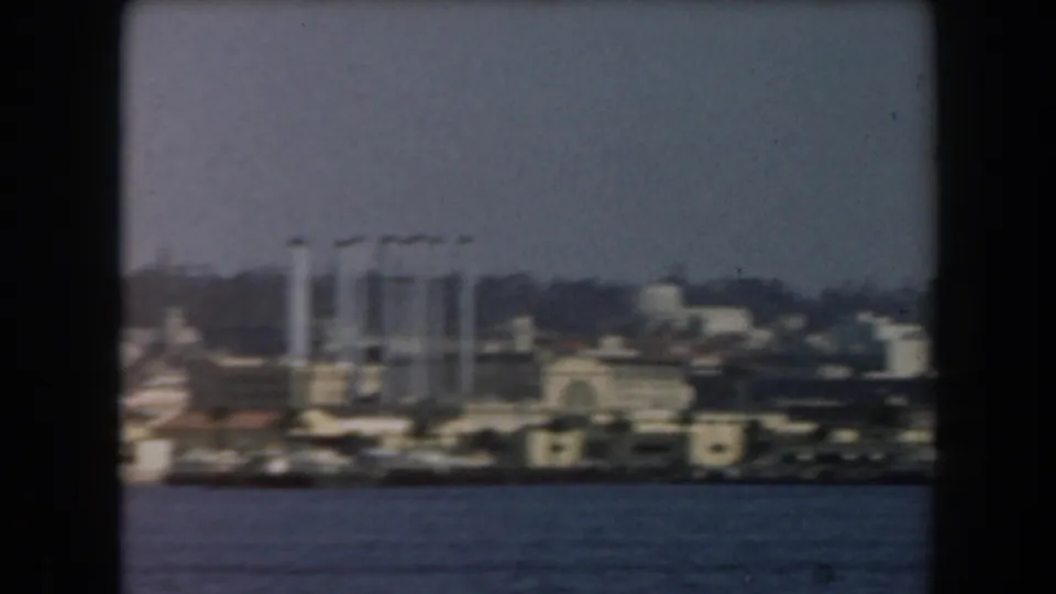 Mid-century California port view with white vertical structures, shoreline buildings, and water in the foreground.